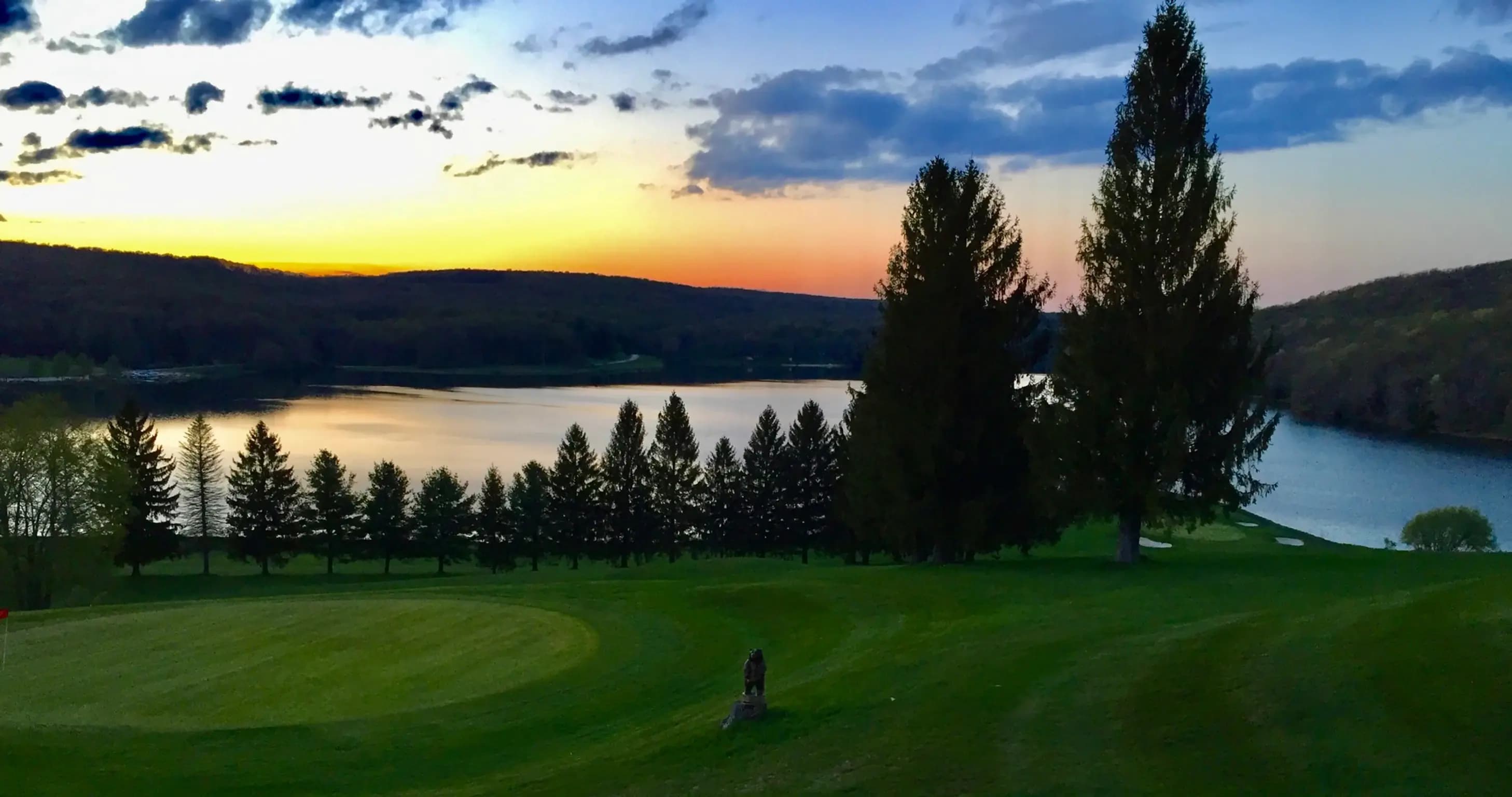 A serene golf course at sunset, surrounded by lush trees and shimmering water